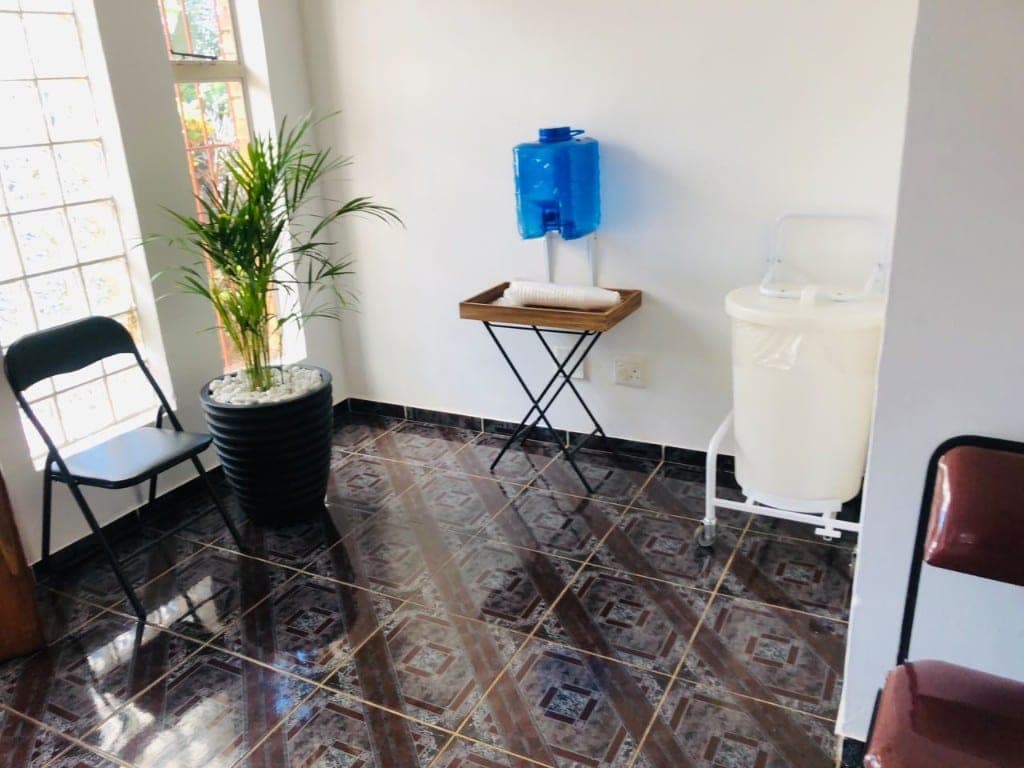 Clinic waiting corner with seating, plant, and water station at Elshaddai Health Care Centre