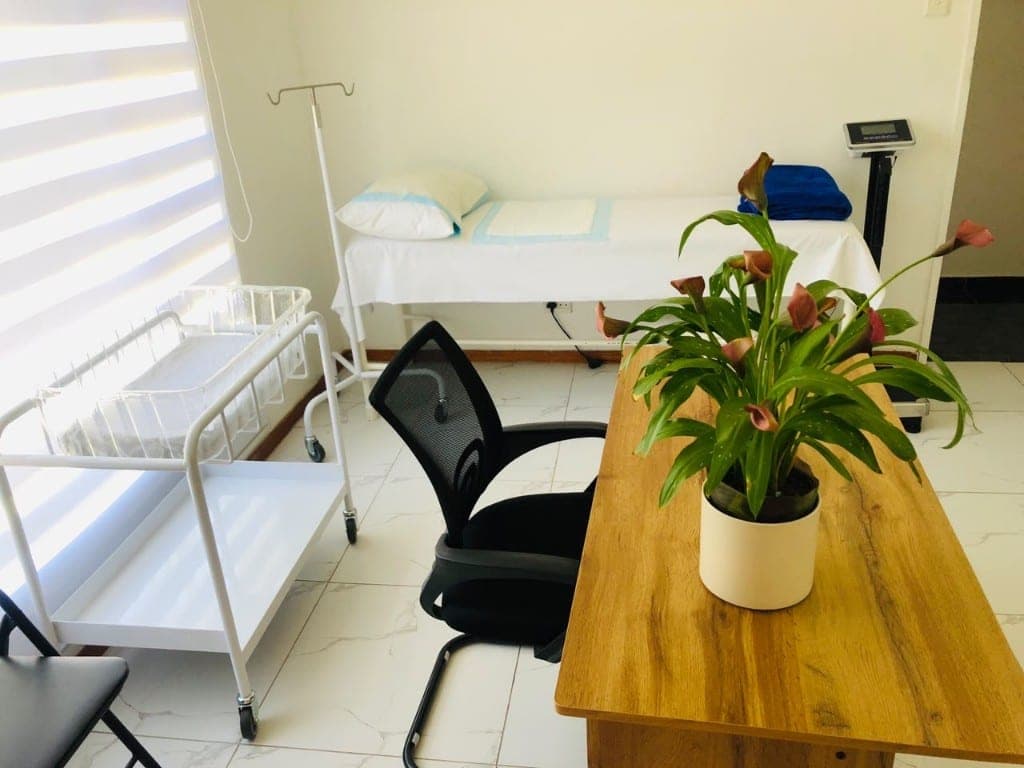 Private consultation room with examination bed and infant bassinet at Elshaddai Health Care Centre